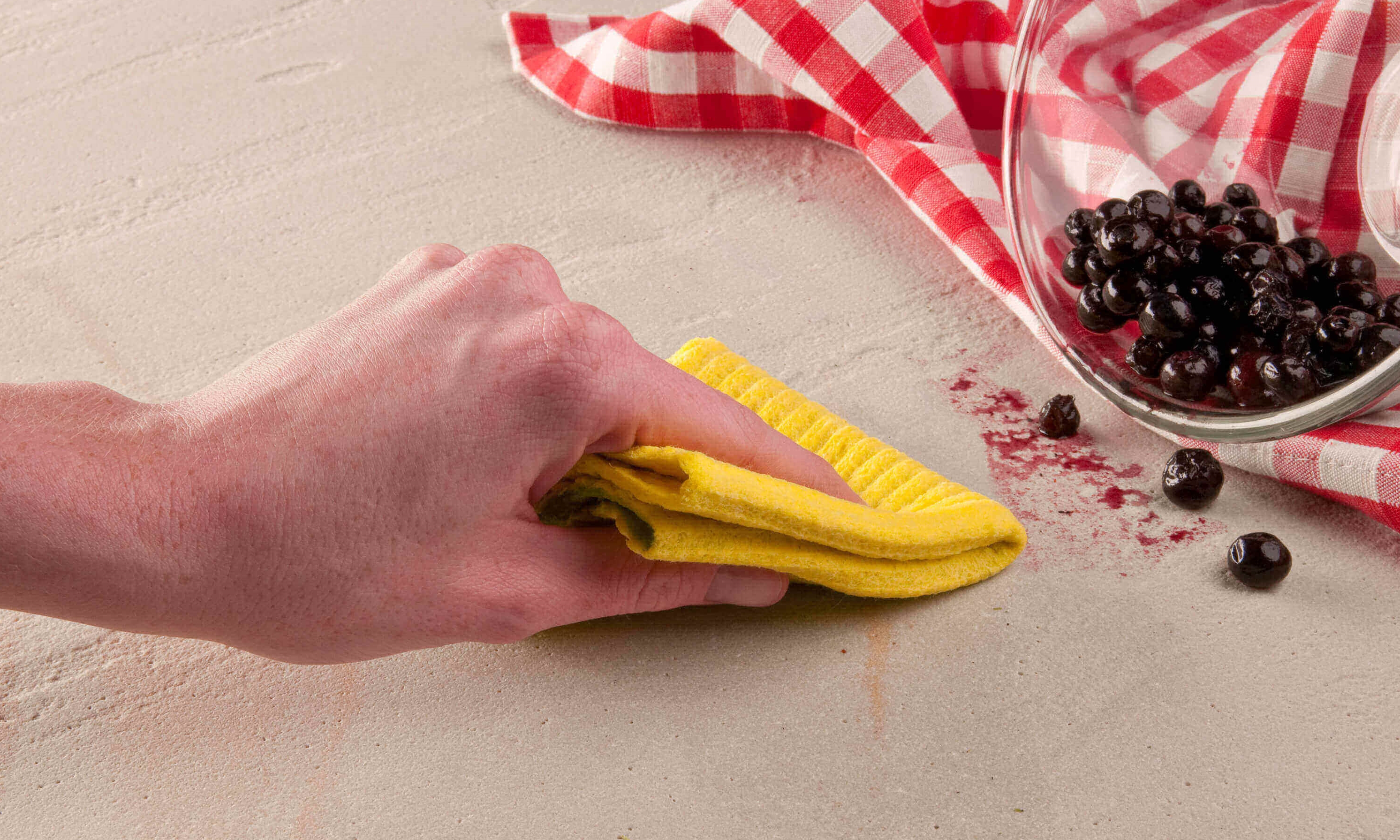 Une main essuie la tache de baie avec un chiffon jaune