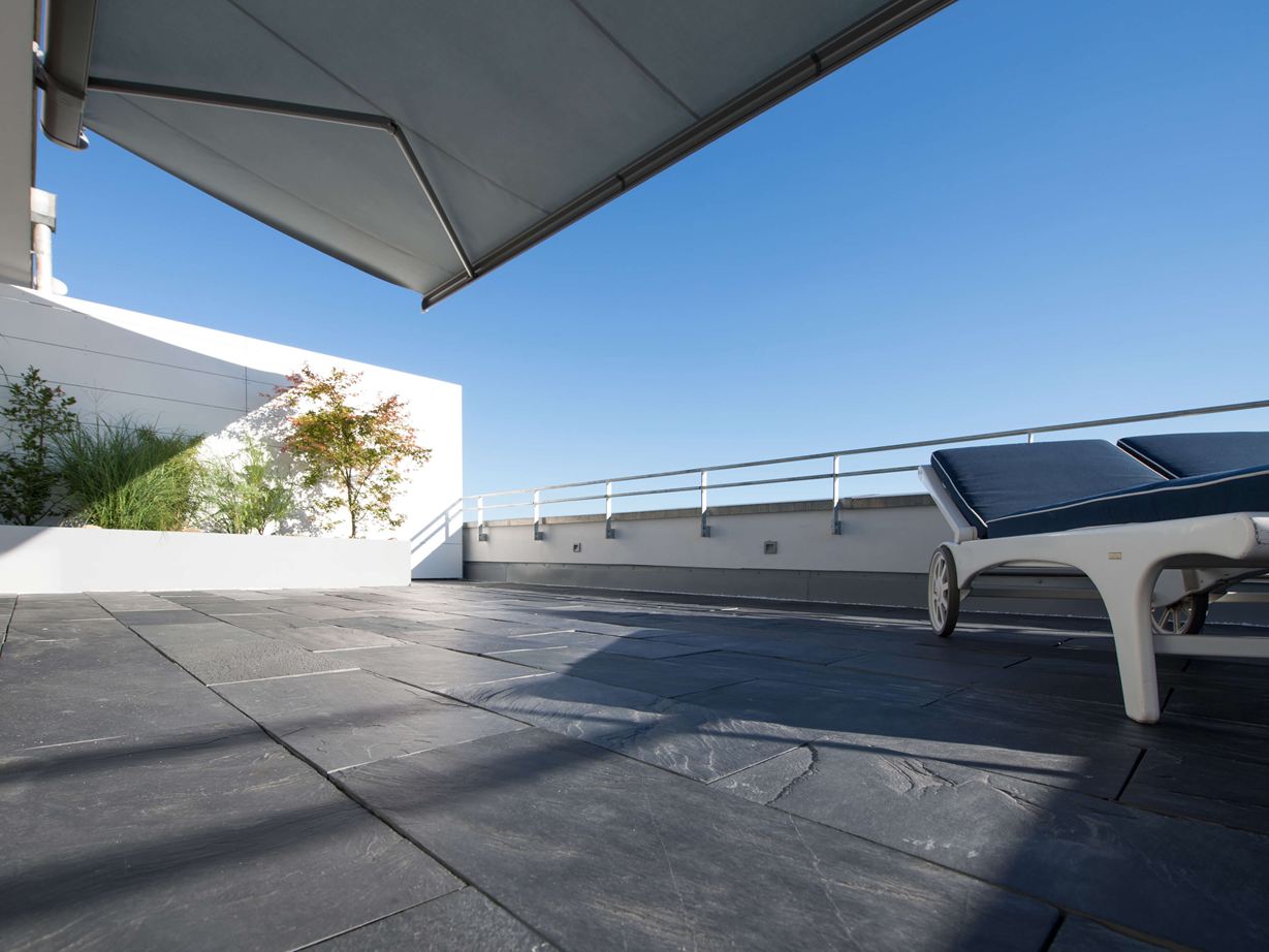 Au soleil, les délitements de l’ardoise sont sublimés. Terrasse sur le toit avec revêtement de sol en ardoise et chaises longues au bord du toit en contre-plongée