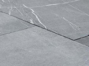 Le style volontairement usé du dallage le rend unique Dalles de pierre calcaire Blaustein Azur en gros plan, des grains blancs sont visibles dans le ton gris clair de la pierre naturelle.