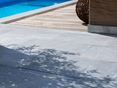 Dalles de calcaire d'un gris tendre au bord de la piscine avc ombres de plantes