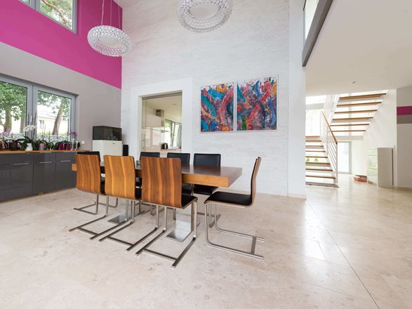 Salle à manger ouverte avec chaises modernes en bois et tableaux colorés au mur, rêvetement de sol en travertin clair à la surface adoucie