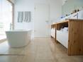 Le travertin se marie bien avec un mobilier en bois. Salle de bain moderne avec commode en bois et baignoire autoportante, carrelage travertin clair au sol.