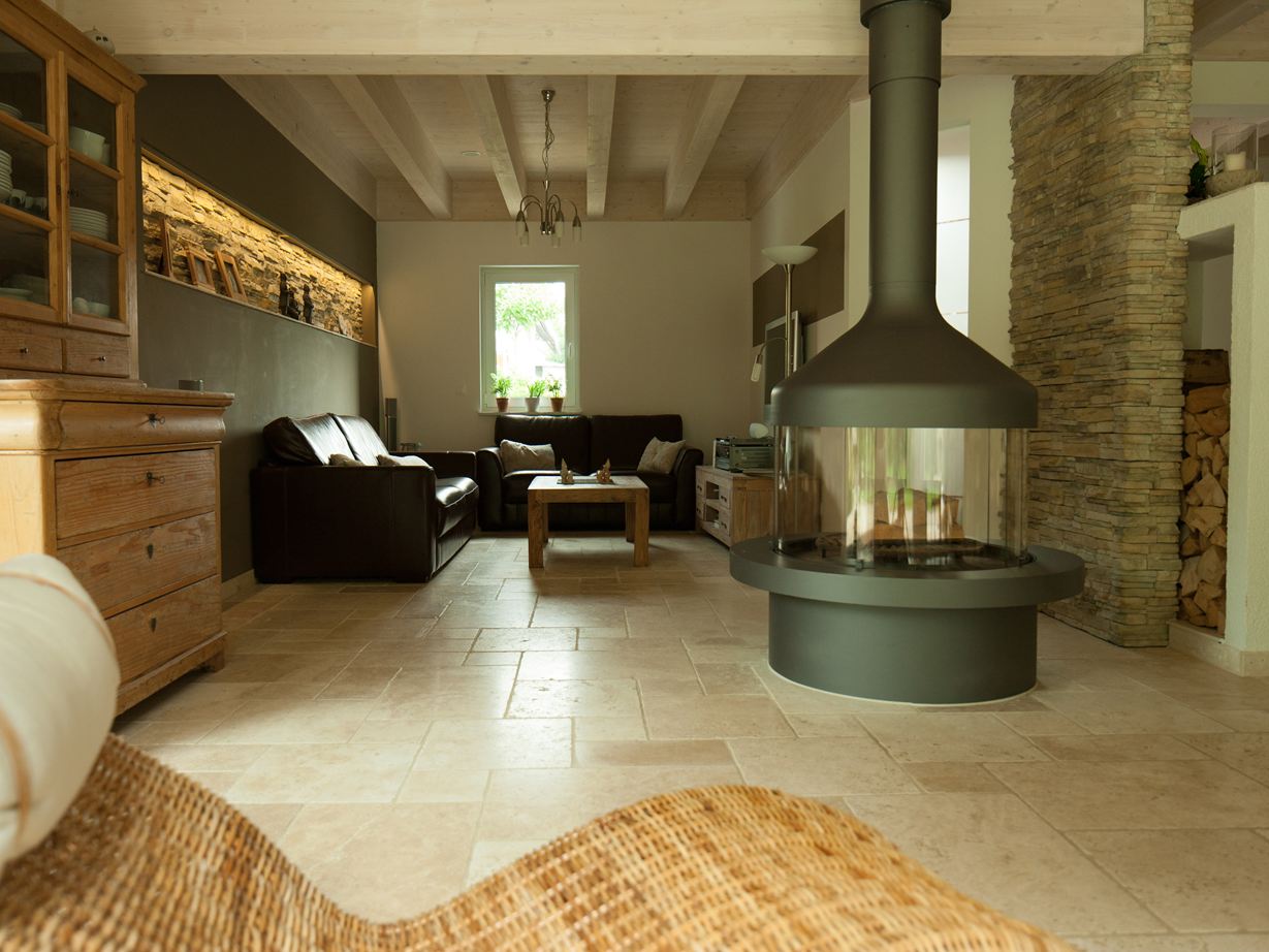 Un salon avec une chéminée sur un sol en travertin Light, au premier plan, un fauteuil