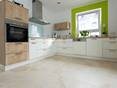 Beige & blanc : harmonie dans la cuisine. Une cuisine blanche avec des éléments en bois et des fenêtres vertes sur un travertin Light, tambouriné