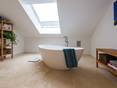 Les couleurs claires créent une ambiance relaxante. Salle de bains avec meubles en bois et baignoire sur carrelage travertin.