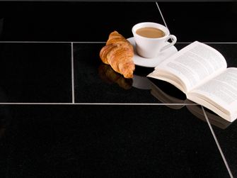 Dunkle Granit-Fliesen Nero Assoluto mit Croissant, Kaffeetasse und einem aufgeschlagenen Buch