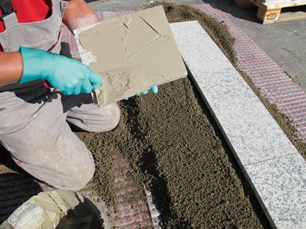 Un installateur applique un adhésif au dos de la pierre pour la pose avec du mortier monogranulaire sur une base de gravier