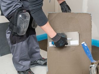 Un carreleur enduit un carreau par l'arrière avec de la colle