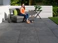 Femme assise sur un fauteuil moderne sur une terrasse avec des dalles en effet ardoise.