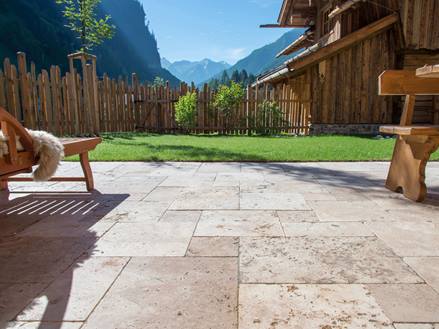 Terrasse au sol avec des meubles rustiques en travertin et en bois, en arrière-plan une pelouse et une vue sur les montagnes