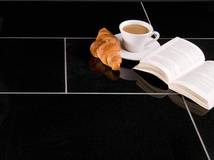une tasse de café, un croissant et un livre ouvert sur des carreaux de granit foncé avec des joints clairs
